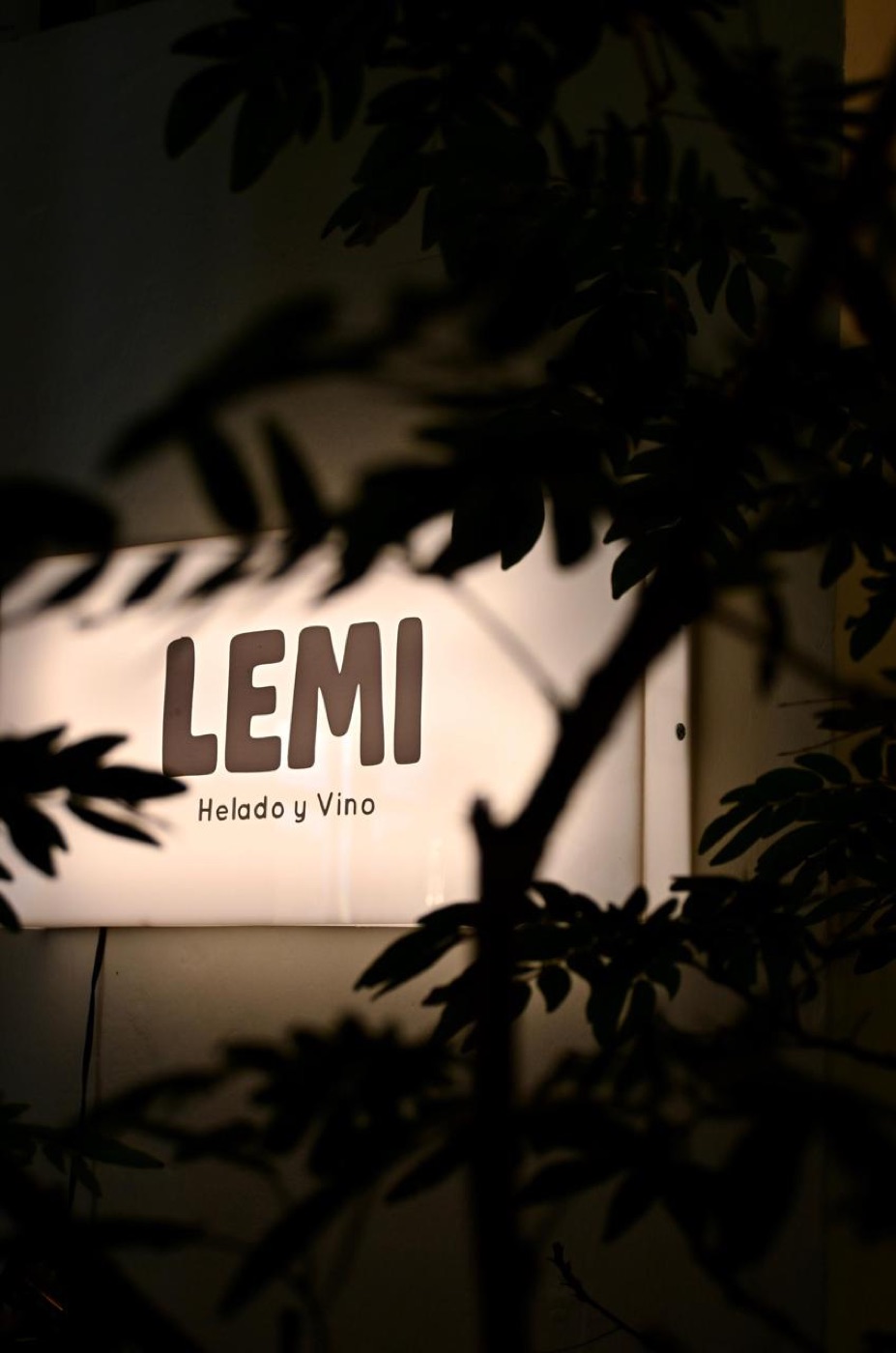 Letrero iluminado de LEMI entre hojas, de noche