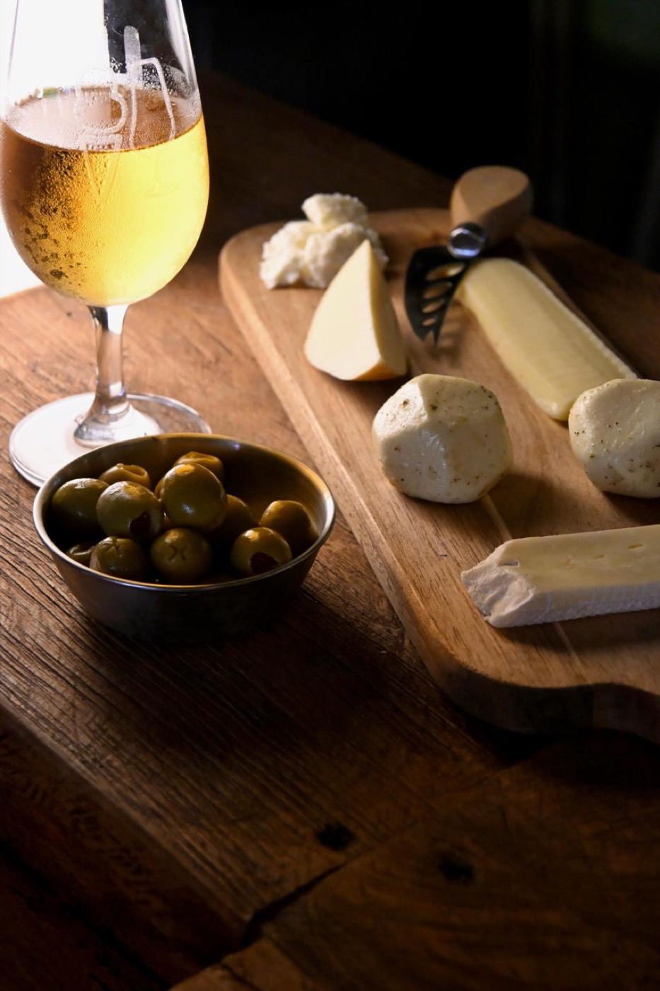 Tabla de quesos con aceitunas y copa de vino blanco